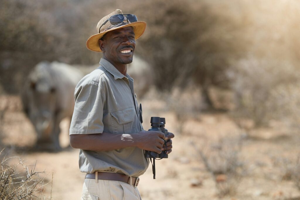 Portrait of a confident game ranger looking at a group of rhinos in the veld